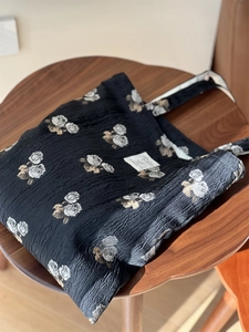 Macro detail of black floral jacquard tote bag featuring rose embroidery on wooden stool