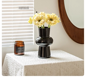 Detail of a vintage-style black stacked glass vase with flowers on a textured table