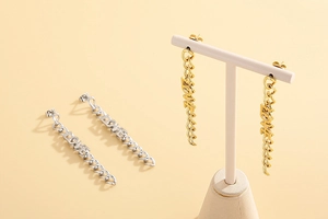 Detail showing gold and silver LOVE long chain drop earrings on a jewelry display stand