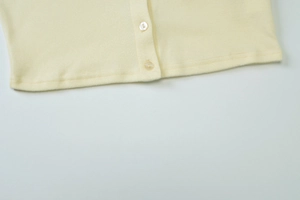 Detail view of light yellow knit cardigan featuring pearlescent buttons and hemline texture