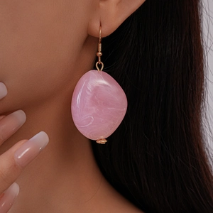 Macro view of pink marble texture resin earrings with golden hooks worn by a model