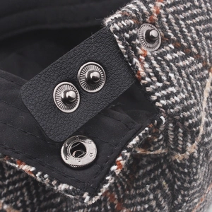 Macro detail of men's wool tweed newsboy cap with leather strap and metal snaps