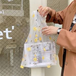 Chic mesh tote bag with yellow floral embroidery held by a model in a brown blazer