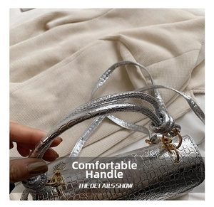 Close-up of silver crocodile embossed handbag featuring a knotted handle and gold hardware