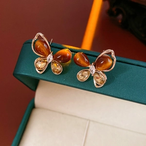 Macro detail of butterfly earrings with amber tiger eye stones on green leather box