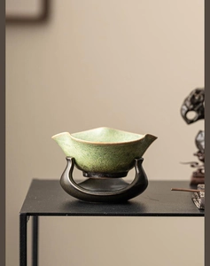 Detailed view of a green glazed ceramic tea strainer with an artistic U-shaped dark base