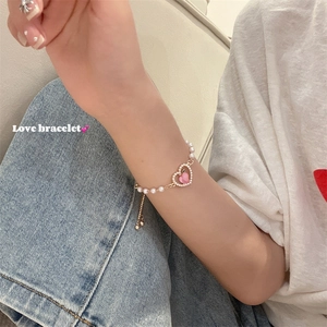 Dettaglio del bracciale con perle regolabile e ciondolo a cuore color pesca sul polso
