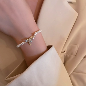 Detail shot of a baroque pearl bracelet with a gold zircon bow charm on a woman wrist