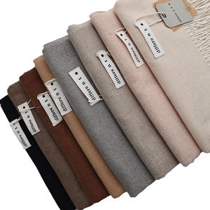 Stack of solid colored cashmere feel scarves with tassel trim and woven textures