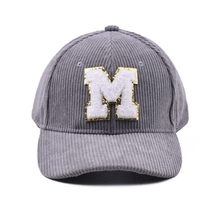 Detail der grauen Cord-Baseballkappe mit Plüsch-M-Patch und goldenen Paillettenstickereien