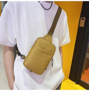 Detail of a ginger yellow canvas crossbody bag with olive green nylon strap worn by a model