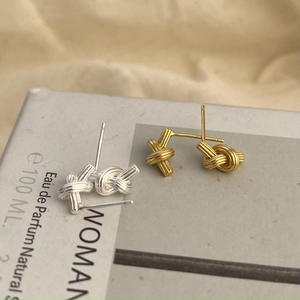 Close-up of minimalist gold and silver knot earrings on aesthetic lifestyle background