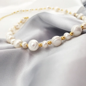 Close-up of baroque freshwater pearls and gold beads on soft grey silk fabric background