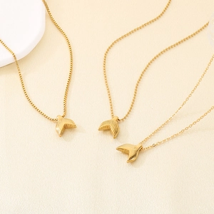 Detailed view of three golden fishtail pendant necklaces with hammered texture on beige surface