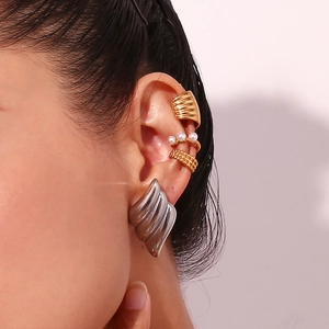 Close-up of stacked gold ear cuffs and a silver wavy hoop earring with pearl accents