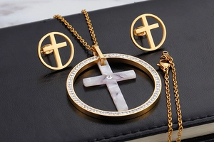Macro detail of golden necklace and earrings with marble cross inlay and white rhinestones