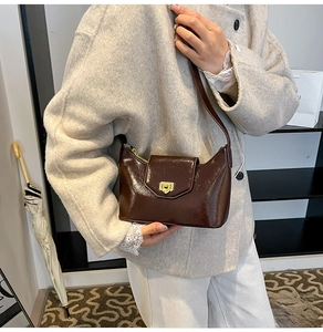 Detail view of glossy dark brown crescent bag with gold rotary lock and leather strap