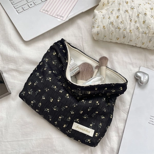 Vue à plat d'une trousse à maquillage en toile fleurie sur un lit avec accessoires