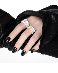 Detailed view of silver textured rings with gold accents on model with black nails