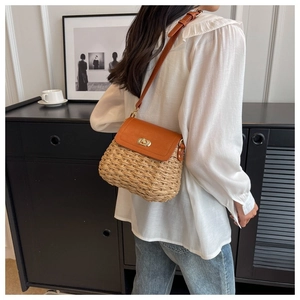 Close-up of a handmade straw crossbody bag with orange leather flap and metal clasp