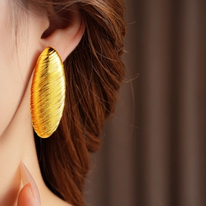 Close-up of oversized gold textured oval earring worn by a model for a vintage look