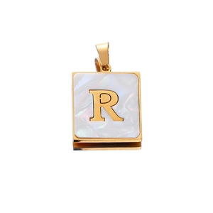 Detail of square gold pendant with white shell inlay and 3D metallic letter R