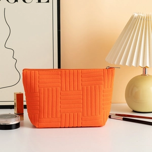 Detail of orange textured stripe cosmetic bag with zipper on a minimalist white vanity