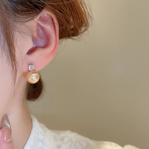 Close-up of elegant gold pearl earring with zircon inlay worn by model in soft lighting