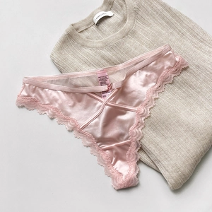Close-up of pink satin panties with delicate lace edges and heart detail on a soft sweater