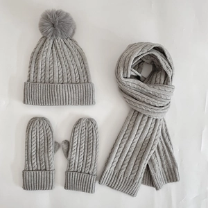 Detail of grey cable knit set including pompom beanie, scarf and gloves for winter