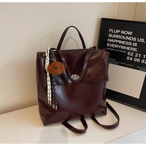 Detail of burgundy PU leather backpack with plush dog charm and woven strap detail