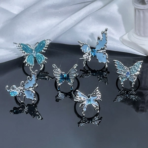 Detailed view of silver butterfly rings with blue gemstones on a silk and marble base