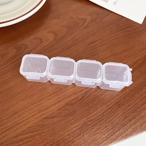 Close-up of portable transparent 4-slot plastic jewelry box on dark wood surface
