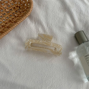 Detail of medium marble-textured hair claw clip on white fabric with lifestyle decor
