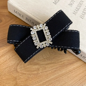 Detail view of black velvet bow hair clip with luxury rhinestone centerpiece on book