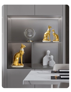 Three gold Egyptian Bastet cat statues in various sizes on a luxury marble table