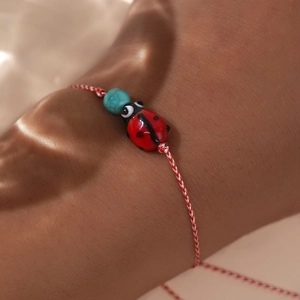 Woven Greek Martis bracelet with red ladybug charm and turquoise bead on wrist