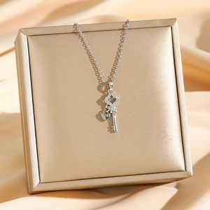 Elegant silver-toned key pendant necklace with crystal accents on a beige satin background