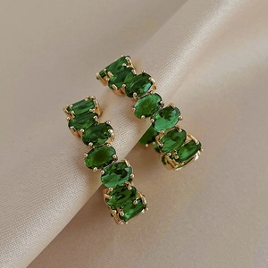Detailed view of gold C-shaped earrings with green oval gemstones on beige silk fabric
