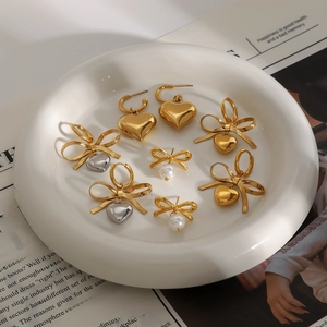 Elegant stainless steel bow and heart earrings collection on white ceramic tray