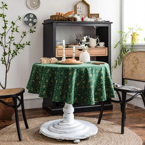 Green Christmas round tablecloth with gold snowflake patterns on a white wooden table