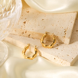 Macro detail of 18K gold-plated twisted croissant earrings on stone and silk background