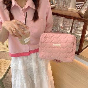 Pink quilted heart cosmetic bag with secure zipper held by a hand in a cafe setting