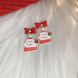 Detail of Christmas earrings featuring red bows, pearls, and snowmen on white fur background