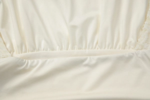 Detailed macro view of cream lace patchwork stitching and fine knit fabric texture