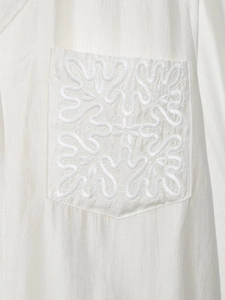 Detailed view of white linen-blend fabric featuring intricate scrollwork embroidery