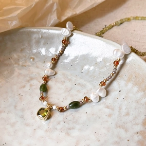 Macro shot of 18k gold plated necklace featuring baroque pearls and green gemstone pendant