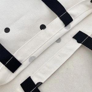 Detail of reinforced stitching on black woven handle of white polka dot canvas tote bag
