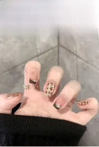 Detailed view of leopard print press-on nails with dark brown French tips and pearl accents