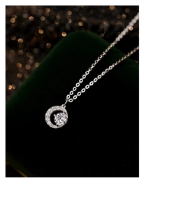 Macro shot of silver crescent moon necklace with zircon stone on green velvet background